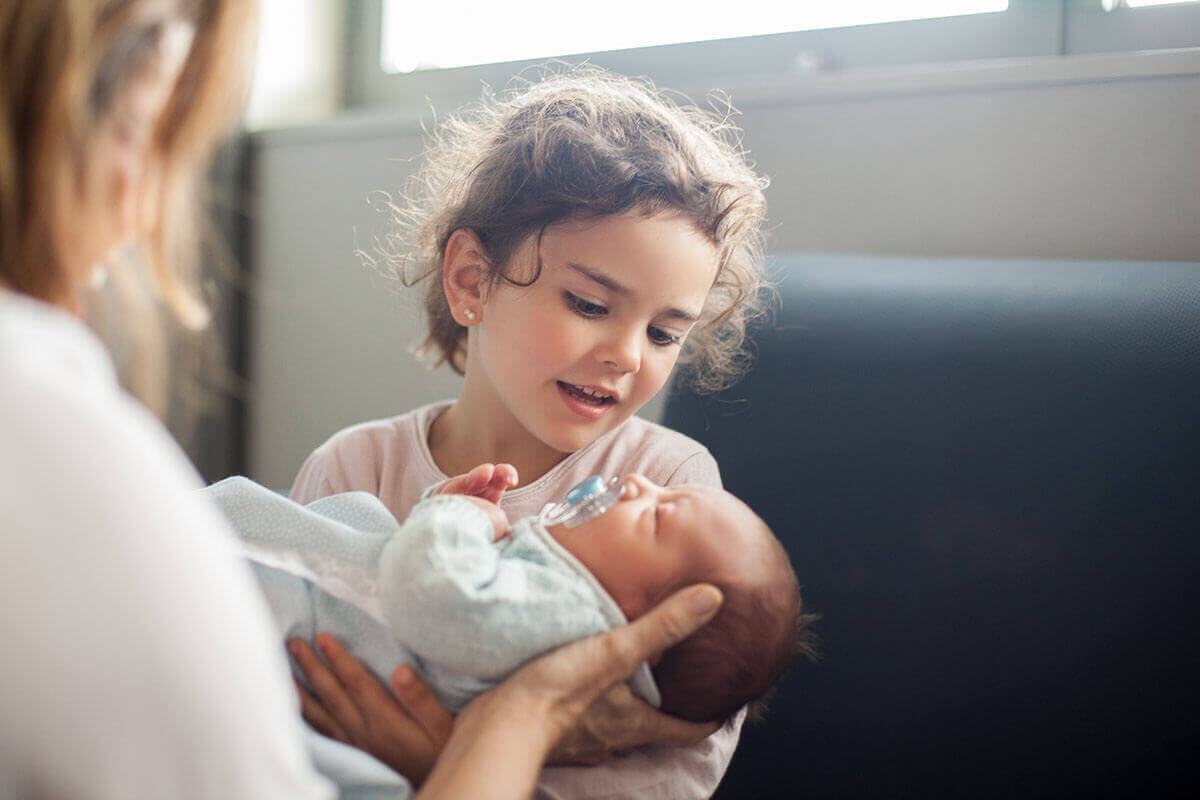 mother-handing-newborn-to-big-sister mother-handing-newborn-to-big-sister